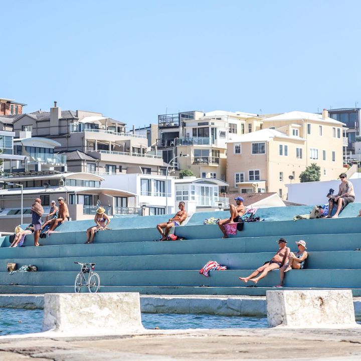 People sit on a tiered concrete seat surrounding an ocean bath